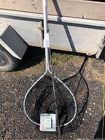 Photo of rubber fishing net with telescoping aluminum handle; fishing rod with reel placed inside the net, leaning against a trailer side panel.