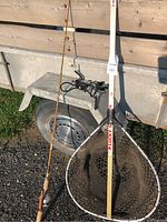 Fishing rod leaning against a wooden surface next to an extending handle rubber fishing net with a ruler for scale.