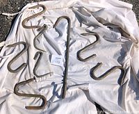 Several assorted metal meat hooks of different sizes and shapes placed on top of a white fabric coat, all showing signs of rust and wear.