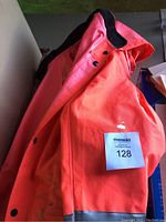 Folded neon orange rain jacket, showing black inner lining and button closure.
