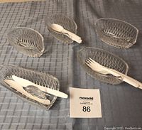 Five clear lead crystal oval-shaped utensil holders on a cloth, each holding white plastic utensils.