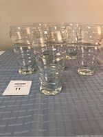 Six tall clear crystal glasses arranged in a loose group on a blue checkered tablecloth, front view.