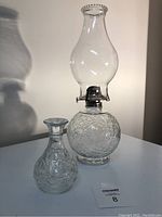 Full view of Princess House Faniansia glass oil lamp and matching vase on white surface showing embossed floral patterns.