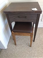 Sewing machine table with a drawer and matching stool pushed underneath.