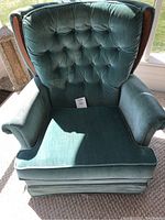 Front view of green velour upholstered rocking swivel armchair showing tufted backrest, seat cushion, and wooden side trim.