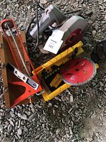 Lot overview showing corded miter saw, extra circular saw blade, two miter boxes, small torpedo level, and caulking gun on gravel surface.