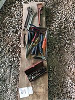 Top view of assorted hand tools and socket set on wooden plank showing adjustable wrenches, pipe wrench, pliers, screwdrivers, and socket case.