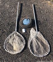 Photo shows both smelt nets and the fish keeper placed on gravel ground, nets with white circular frames and mesh, fish keeper round with blue lid.