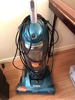 Front view of blue Eureka UNO upright vacuum with power button, clear dust container and cord wrapped around.