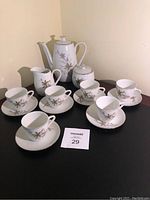 Full view of the vintage mini tea set including teapot, creamer, sugar bowl, 8 cups and saucers on a dark surface against a pale background.