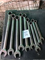 Photo showing nine used metal combination wrenches with open and box ends, laid out on dark textured surface with some rust and wear visible.