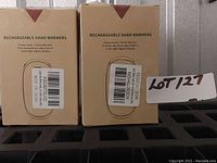 Two boxed rechargeable hand warmers labeled with product info showing five temperature adjustments and cold-light digital displays.