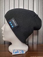 Side profile of black knit elastic toque displayed on mannequin head. Shows Bluetooth control patch sewn on side.