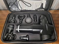 Photo showing the black Carecj massage device and eight different shaped massage heads in a fitted black foam carrying case.