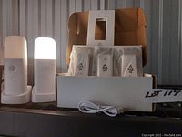 Photo shows two LED night lights illuminated on the left, three additional night lights in plastic bags inside an open white box, an in-wall smart switch, and a USB charging cable in front of the box.