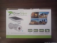 Box front showing Draw Green LED Solar Motion Sensor Lamp with solar panel, highlighting IP66 protection, replaceable battery, lighting timer, and solar rechargeable features.