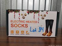 Front of the packaging box displaying 'Electric Heated Socks' with claims of washable, breathable, keep warm, and absorbent materials.