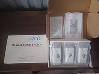 Set of three white in-wall smart light switches in protective plastic with original packaging and instruction manual on a table.