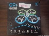 Front packaging photo showing drone model Q9s with 2.4 GHz 4CH remote control. Features listed on box include speed control, lighting mode, 3-axis gyroscope, altitude hold, headless mode, 3D flips, and one key return.