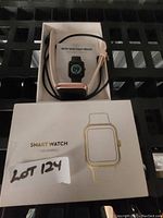 Photo of the B9201 mini Smart Watch with black and pink silicone strap sitting inside a white box with the watch covering some parts of the box. The box cover is shown with a printed outline illustration of the watch.