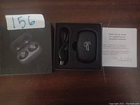 Opened box displaying wireless earbuds charging case, USB charging cable, packaging box, and a small card with customer service information.