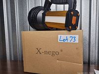 Photos showing the large black and gold X-nego flashlight placed on top of its branded box labeled 'X-nego' with lot number sticker.