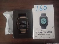 Smart watch in retail packaging with box showing watch face design and branding.
