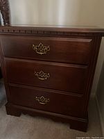 Front view of Broyhill cherry nightstand showing three drawers and brass handles, highlighting condition and design details.