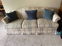 Front view of the beige and blue striped fabric sofa with three blue pillows on the seat cushions.