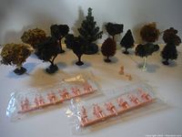 Various model trees arranged in rows with two sets of pink miniature figures in front.