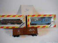 Two Lionel HO scale train cars in original packaging with red and yellow striped borders; one brown Canadian National freight car, one blue locomotive.