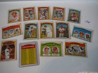 Photo showing 14 baseball cards arranged on a surface, including players in various poses, team lineups, and one checklist card.