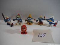 Front view of six Smurf figures arranged in a row including blue and red Smurfs with different accessories and costumes.