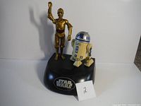 Front view of animatronic Star Wars bank featuring R2-D2 and C-3PO on a black base with Star Wars logo plaque