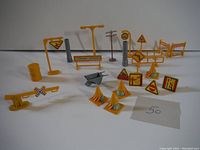 Overview of 24 miniature railway construction signs and accessories arranged on white background showing cones, signs, gates, poles and tools for railway construction play or display.