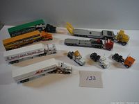 Photo showing all semi truck and trailer toy models laid out with some trailers attached to cabs and some cabs alone. Various colors and logos on trailers visible.
