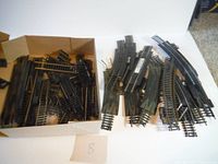 Photo showing box filled with assorted model train track sections, including various types such as straight tracks, curved tracks, switch turnouts, and derailers.