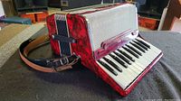 Front view of red pearloid accordion with leather straps attached, showing keys and grille