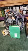 Sprayer unit with coiled hose, spray gun, green-foldered manual and accessory case visible in front of paint cans