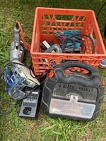 Various used Black & Decker corded tools together with a charger and a storage crate on the grass.