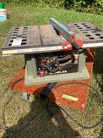 Overall view of Delta table saw on dolly outdoors showing front panel, cast iron table top, fence, and power cord.