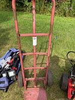 Front view of the red medium duty hand truck showing tubular metal frame, some rust and paint missing.