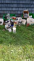 Overview of all hardware items including buckets, containers, and wheels on grass outside a building with shingles.