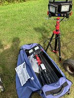 Two LED shop light units on red tripods, blue carrying bag open showing disassembled stands and lights.