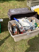 Wide shot of paint supplies in a large plastic bin outdoors showing rollers, trays, and various painting tools.