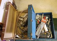 Overview of two open leather suitcases, one containing metal paint sprayer and others packed with paint rolling tools