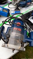 Ryobi plunge router on a white table surrounded by some other tools and accessories.
