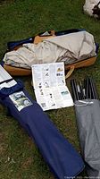 Items laid out on grass showing folded tent, instruction sheet, and two bags containing tent poles and accessories.