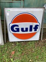 Front view of white square plastic sign with orange circle and blue Gulf logo