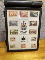 Front view of the framed Canadian Centennial stamp collection showing all 12 stamps arranged around the Canadian coat of arms and Canada Centennial inscription.
